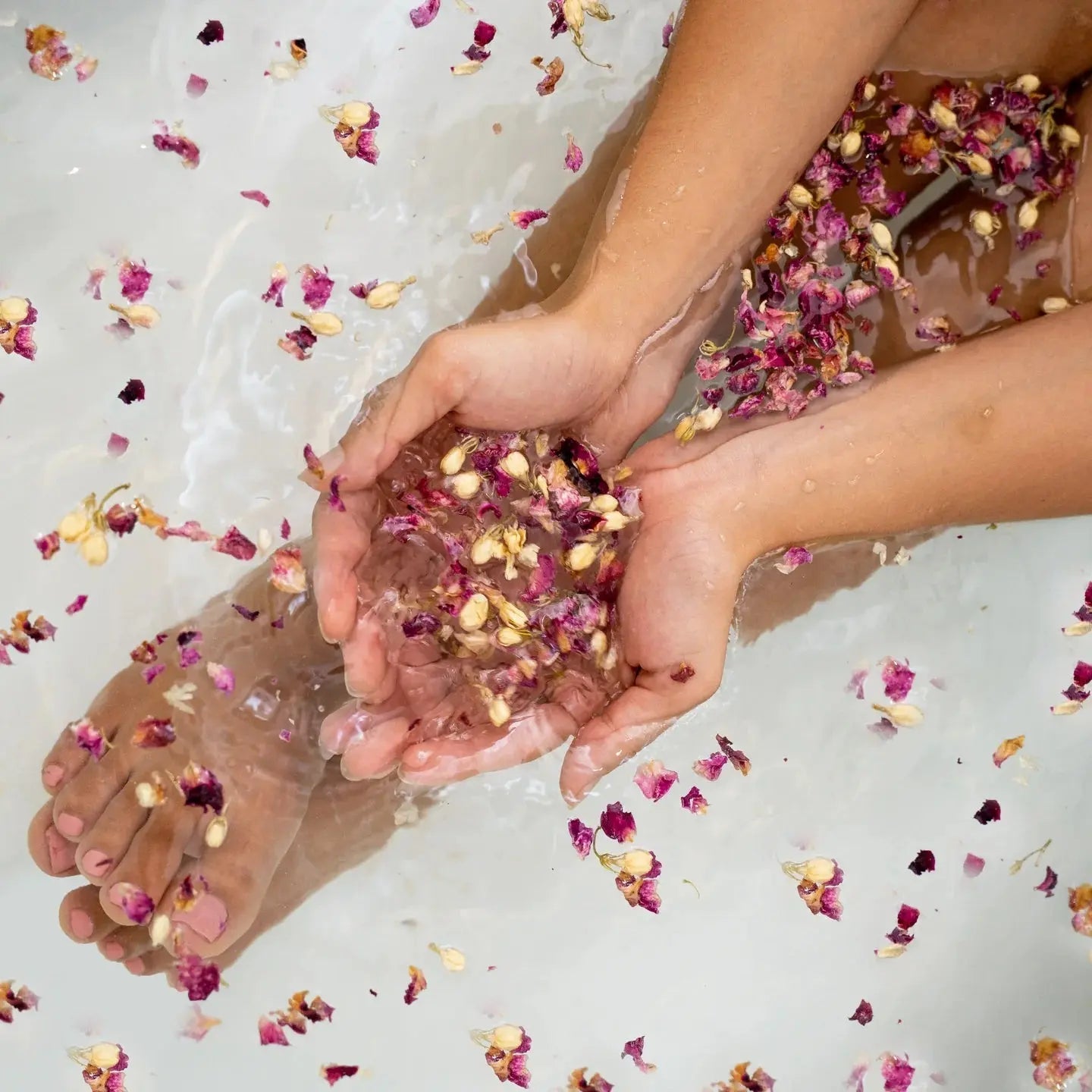 a persona sitting in a body of water with Botanical bath and facial steam florals in the persons hands and bathtub