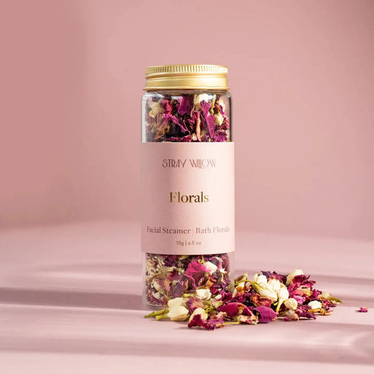 Botanical bath and facial steam bottle filled with dried florals captured with a pink background.