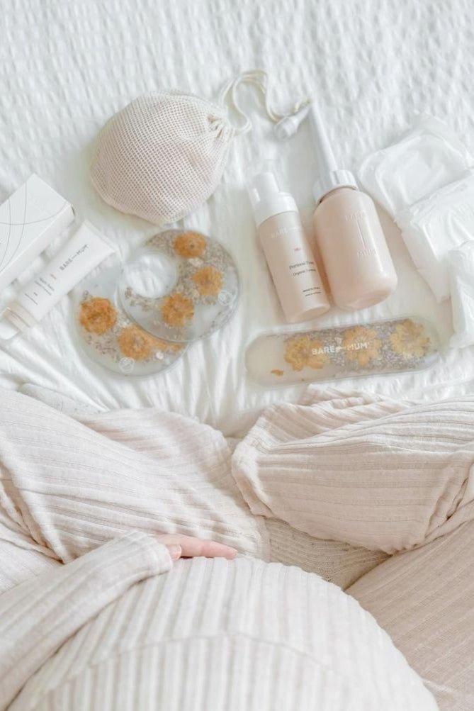 a pregnant person sitting on a bed with postpartum care products